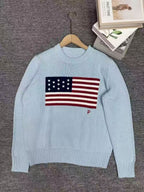 Light blue sweater with American flag design on a hanger against a gray background.