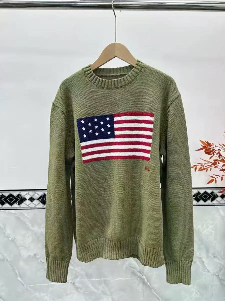 Green sweater with American flag design on a hanger against a white wall.
