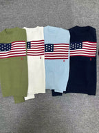 Four sweaters with American flag design on a gray surface