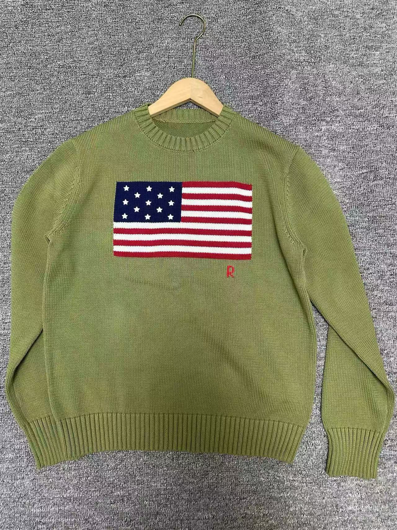 Green sweater with American flag design on a hanger against a gray background