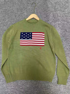 Green sweater with American flag design on a hanger against a gray background