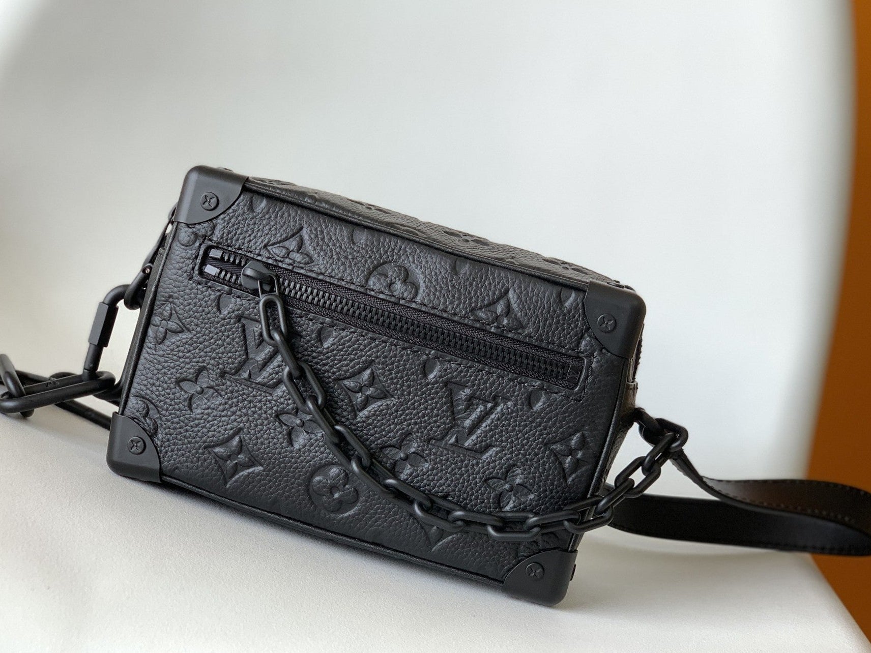 Black textured handbag with chain detail on a white surface