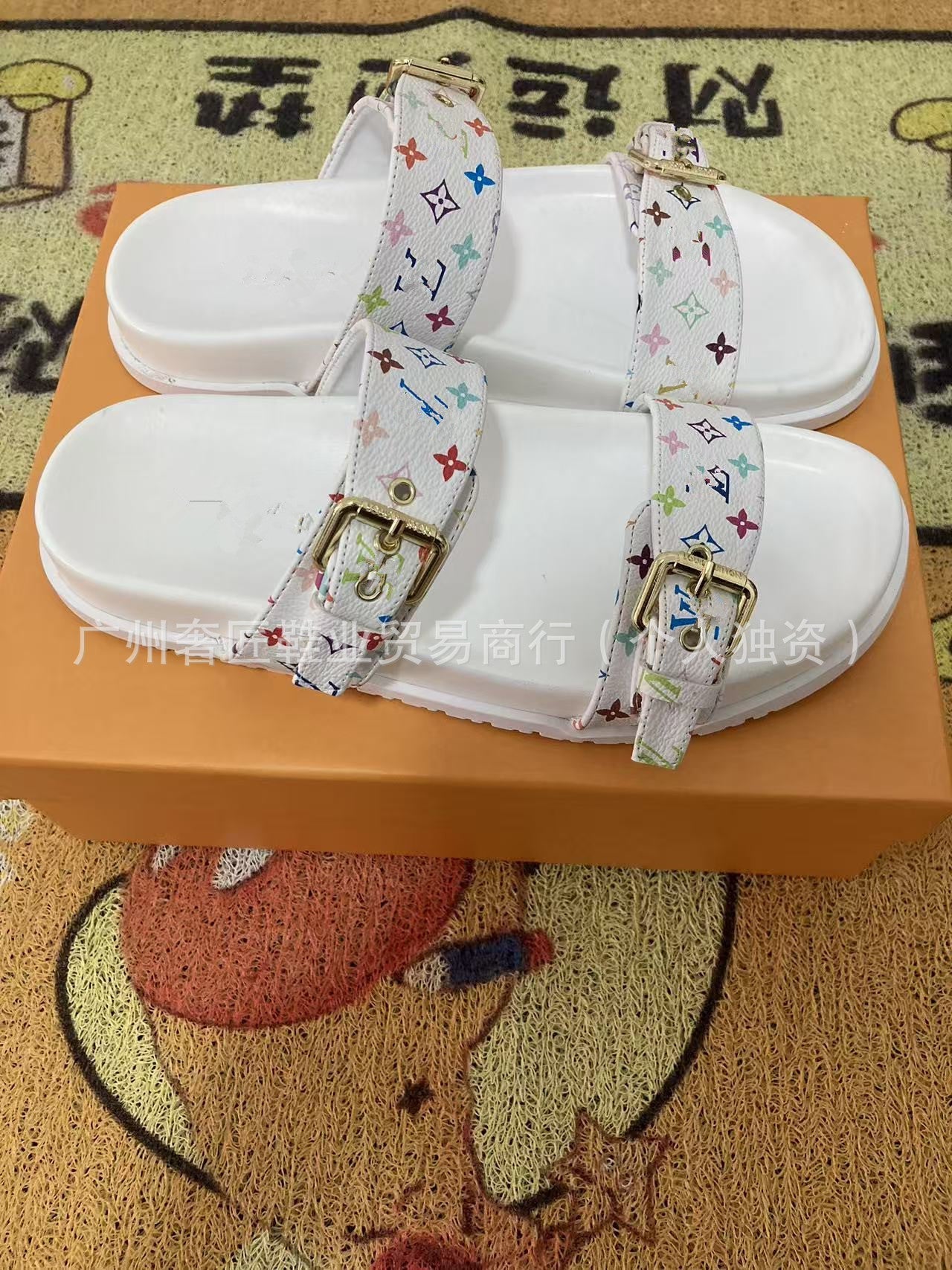 White sandals with colorful straps on an orange box against a patterned background