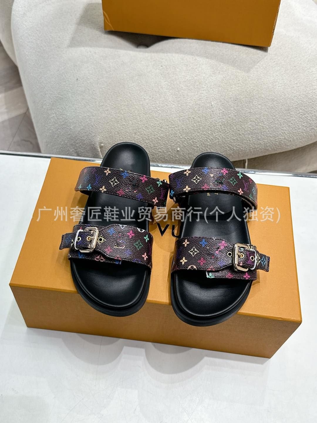 Black sandals with patterned straps on a brown box with visible branding.