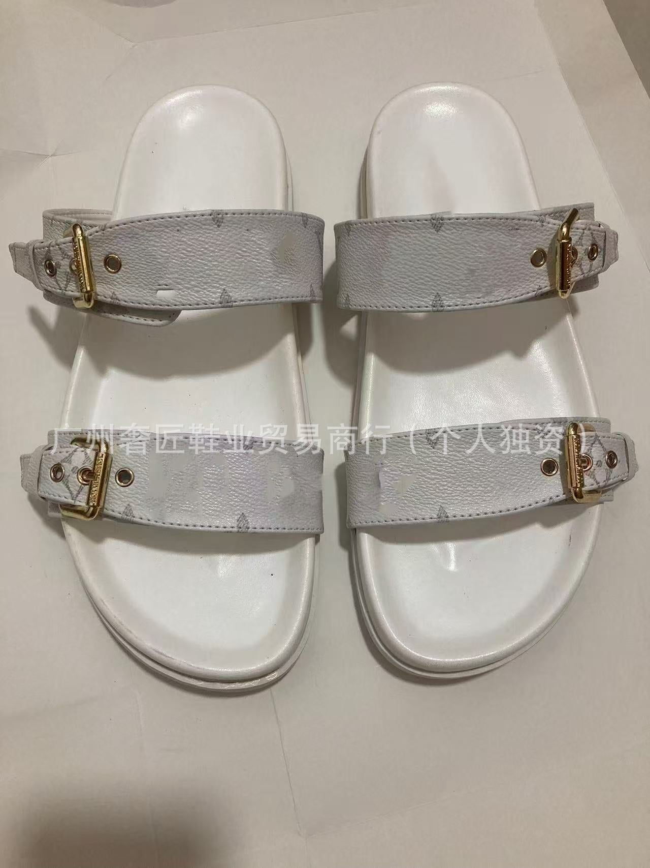 Pair of white sandals with gold buckles on a light gray background