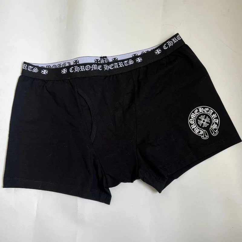 Black boxer briefs with a white embroidered circular logo on the left leg and a white patterned elastic waistband with the brand name 'Chrome Hearts' repeated.