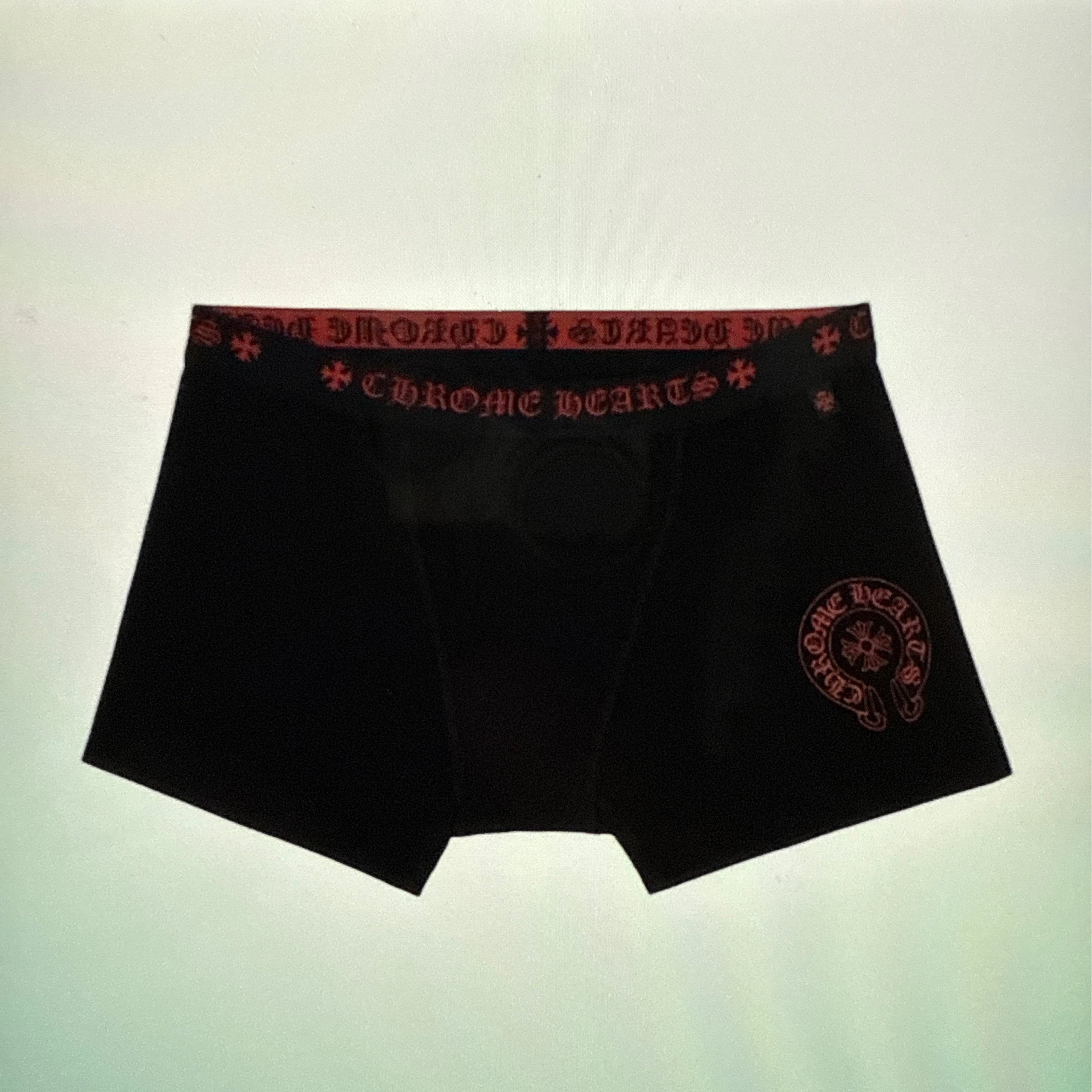 Black boxer briefs with red embroidered 'Chrome Hearts' text on the waistband and a red circular logo patch on the left leg, shown against a pale greenish background.