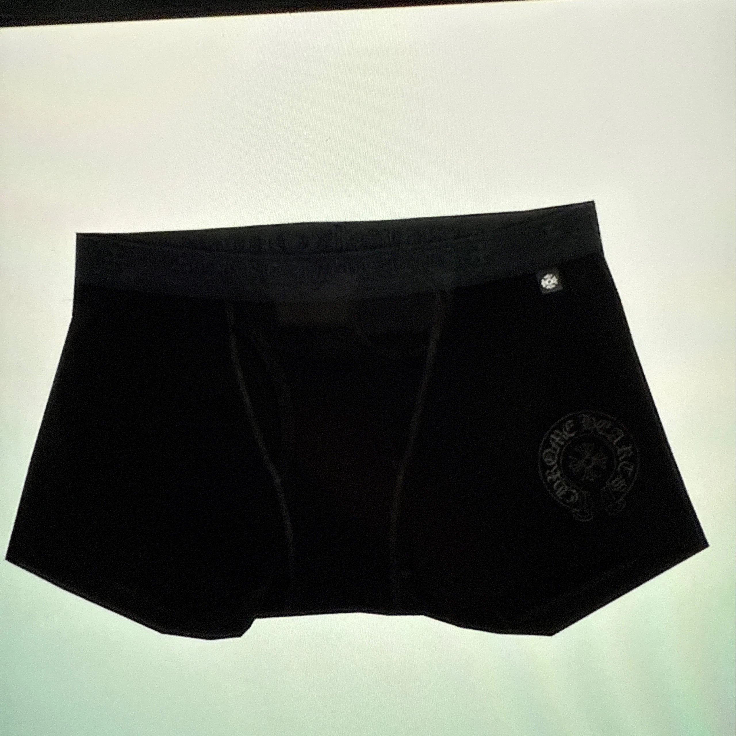 Black boxer briefs with a tonal embroidered Versace logo on the lower right leg and a small silver button closure, shown against a plain light background.