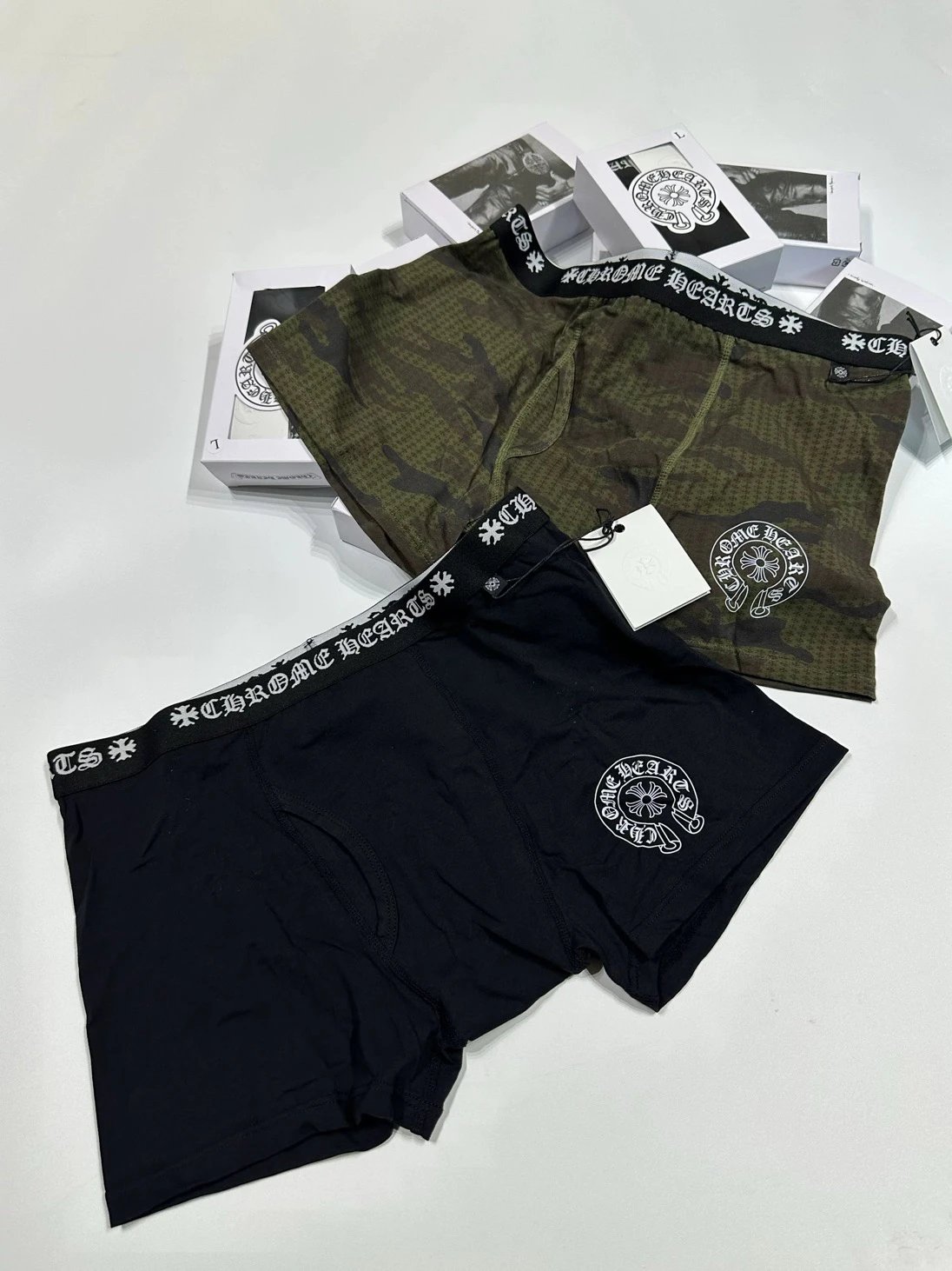Two pairs of boxer briefs, one black and one green with branding, on a white background.