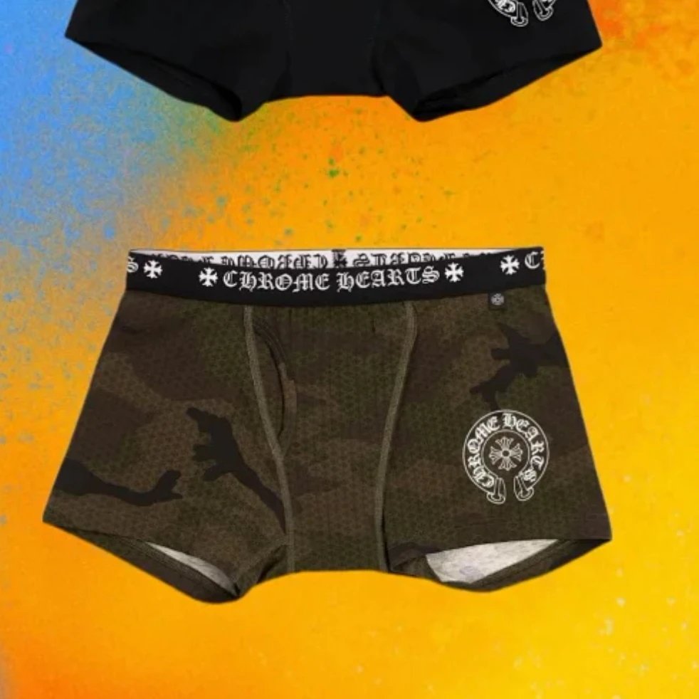 Chrome Hearts boxer briefs in a dark green camouflage pattern with a black elastic waistband featuring the brand name and cross logos, shown alongside another pair of black boxer briefs on a vibrant orange and yellow background.