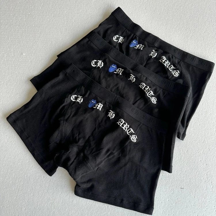 Three pairs of black boxer briefs stacked diagonally on a light gray textured surface. Each pair features white Gothic-style embroidered lettering spelling 'CASH IS KING' alongside a small blue hand icon.