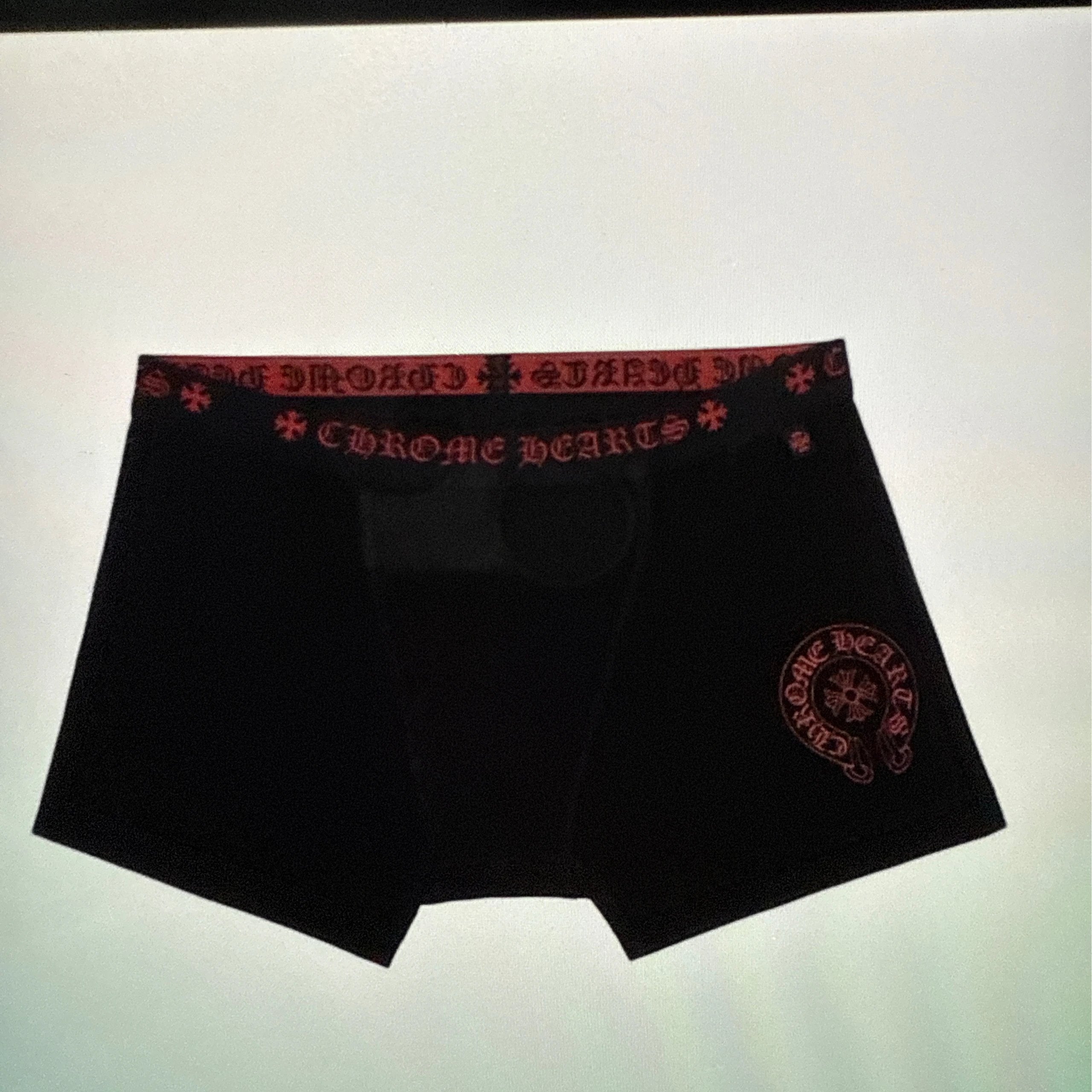 Black boxer briefs with a red patterned waistband and a red circular medallion logo on the lower right leg, shown against a plain light background.