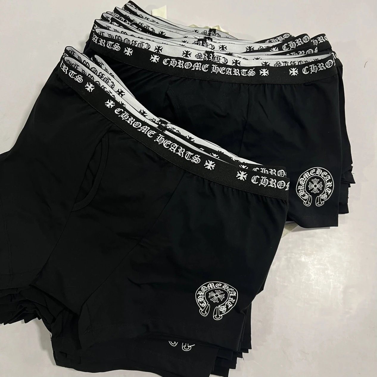 A stack of black boxer briefs with white elastic waistbands featuring the Chrome Hearts logo and wordmark, laid flat on a light surface.