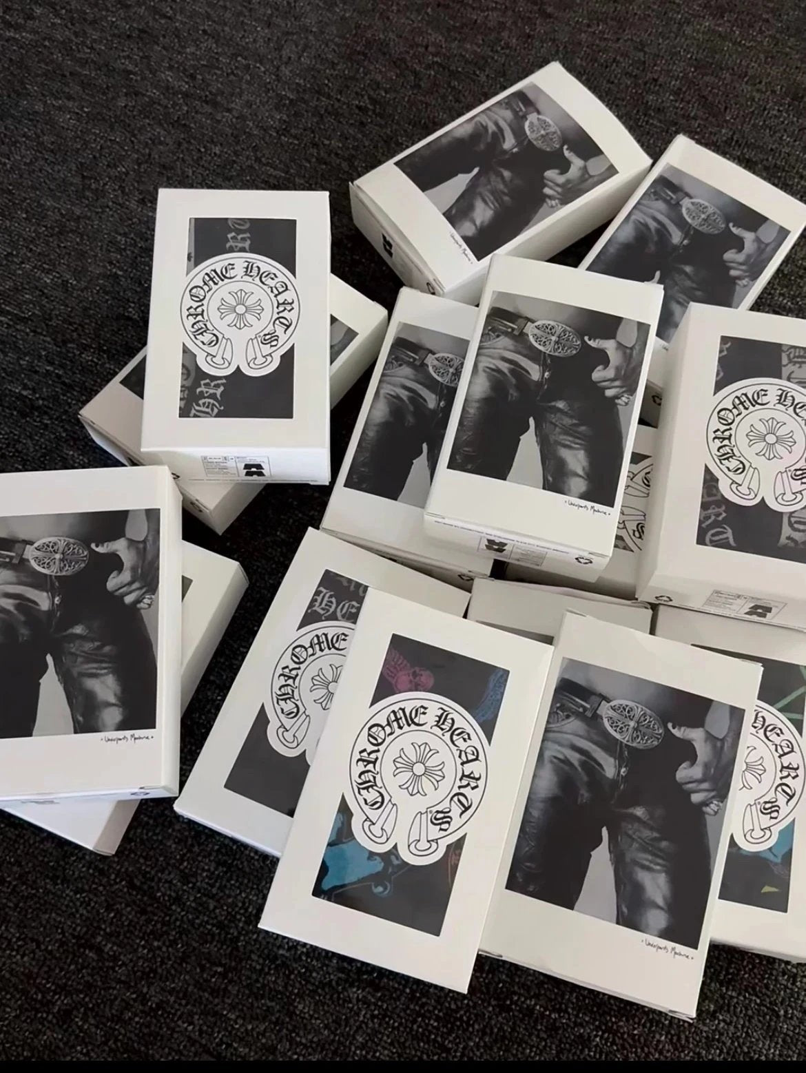 Multiple white boxes of Chrome Hearts jewelry arranged on a dark textured carpet, each showing a black-and-white photo of a person wearing a necklace and the Chrome Hearts logo.