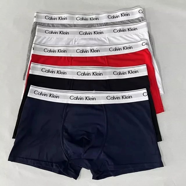 Three pairs of Calvin Klein boxer briefs in black, red, and gray on a light gray background.