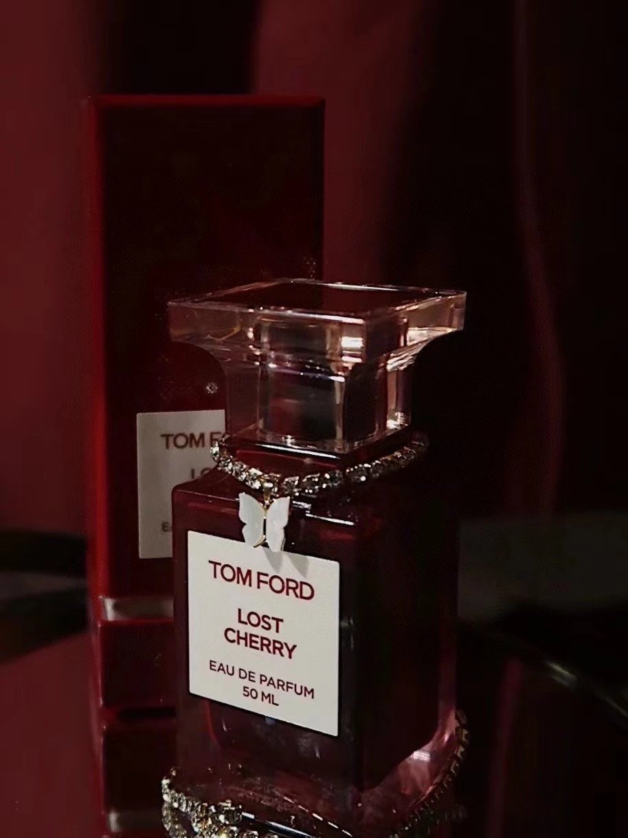 A Tom Ford Lost Cherry Eau de Parfum 50ml bottle with a white label and rhinestone trim, set against a dark red background with its matching red box behind it.